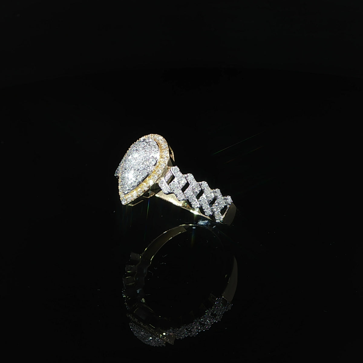 Three-quarter view of a 0.38 CTW natural diamond pear cluster ring in 10K yellow gold on a reflective black surface.