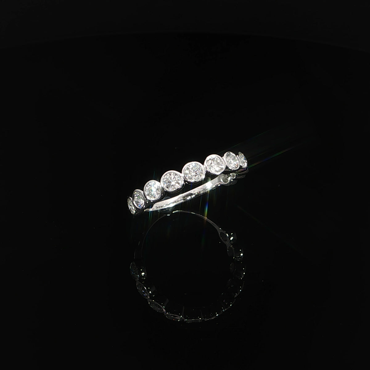 Angled view of a 14K white gold ring with connected round diamond bezels creating a scalloped outline.