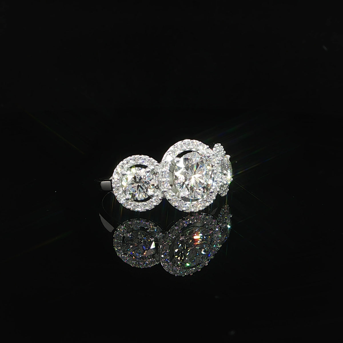 Three-stone setting with a larger round center diamond and two halo-framed side diamonds.