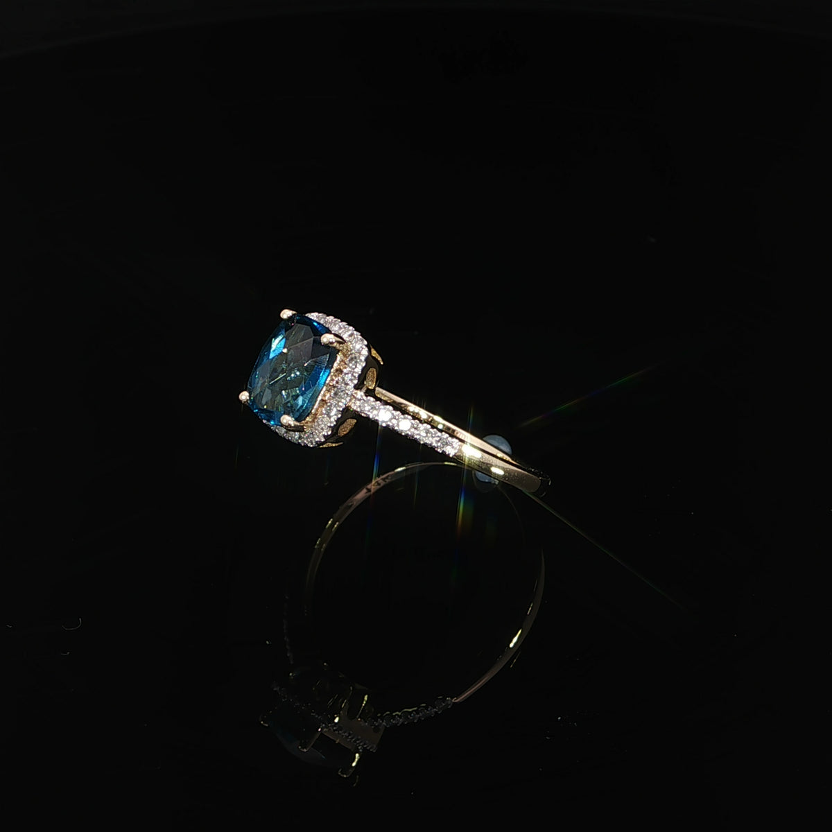 Tilted view of a 7 × 5 mm cushion-cut blue topaz ring in 14K yellow gold with 0.09 CTW diamonds.