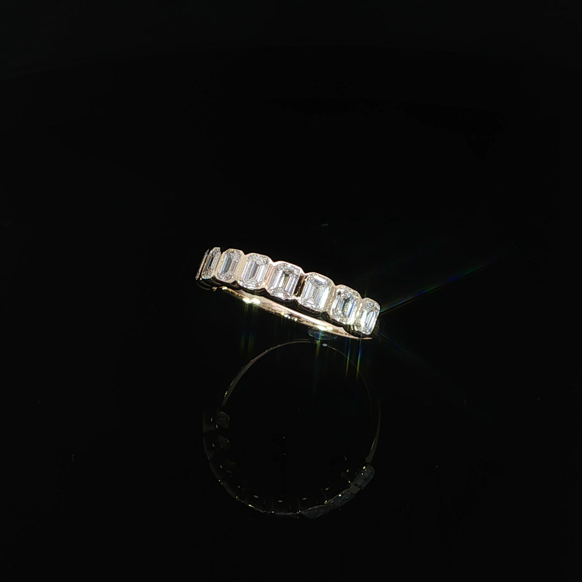 Angled view of a 14K yellow gold band with emerald-cut diamonds in individual bezel settings.