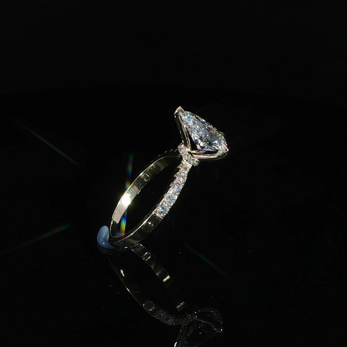 Angled view of a 14K yellow gold engagement ring with a pear center diamond and round band diamonds.