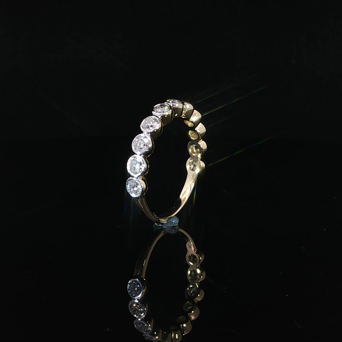 14K yellow gold bezel set diamond band featuring 0.87 CTW round lab grown diamonds in a polished gold setting, photographed at an angle on a black reflective surface.