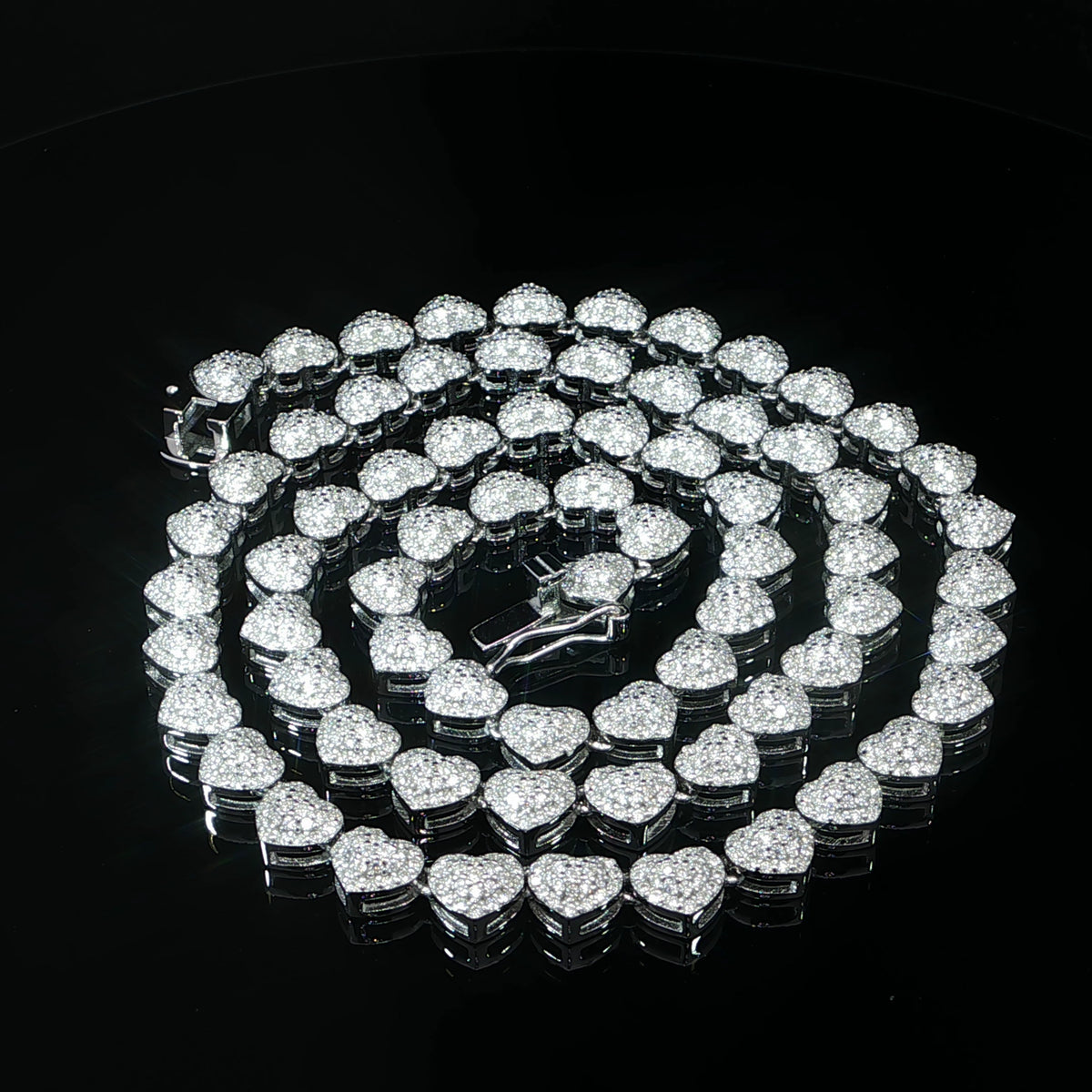 Sterling silver heart halo tennis necklace arranged in a coil on a black background