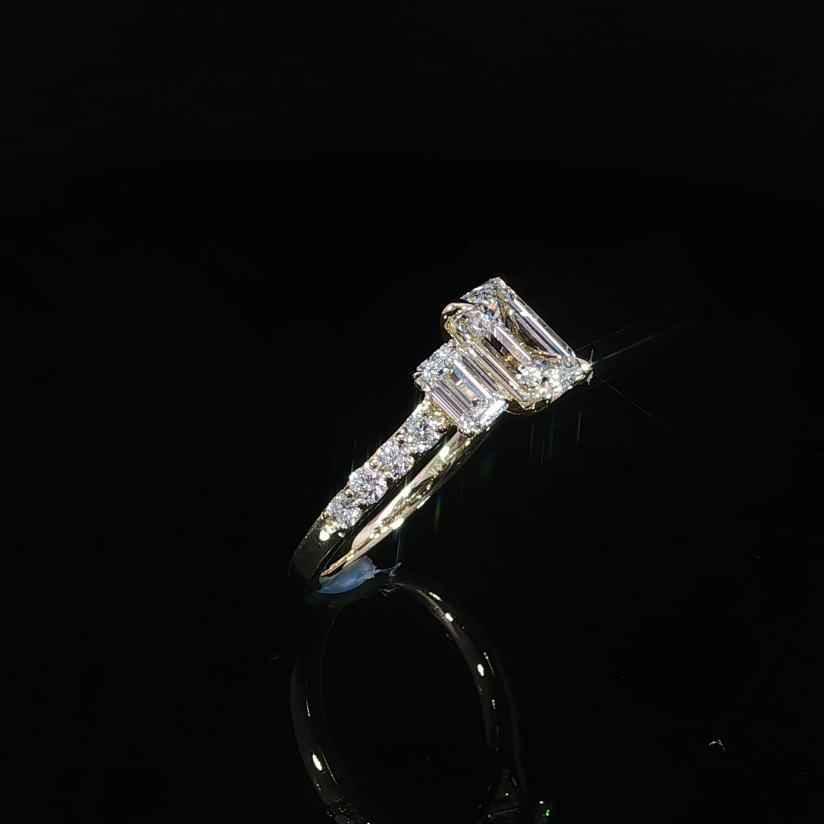 Angled view of an emerald cut diamond ring with side stones and pavé accents in yellow gold.