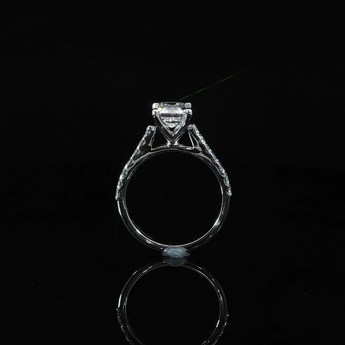 White gold solitaire engagement ring with an emerald cut center diamond and pavé-set shoulders.