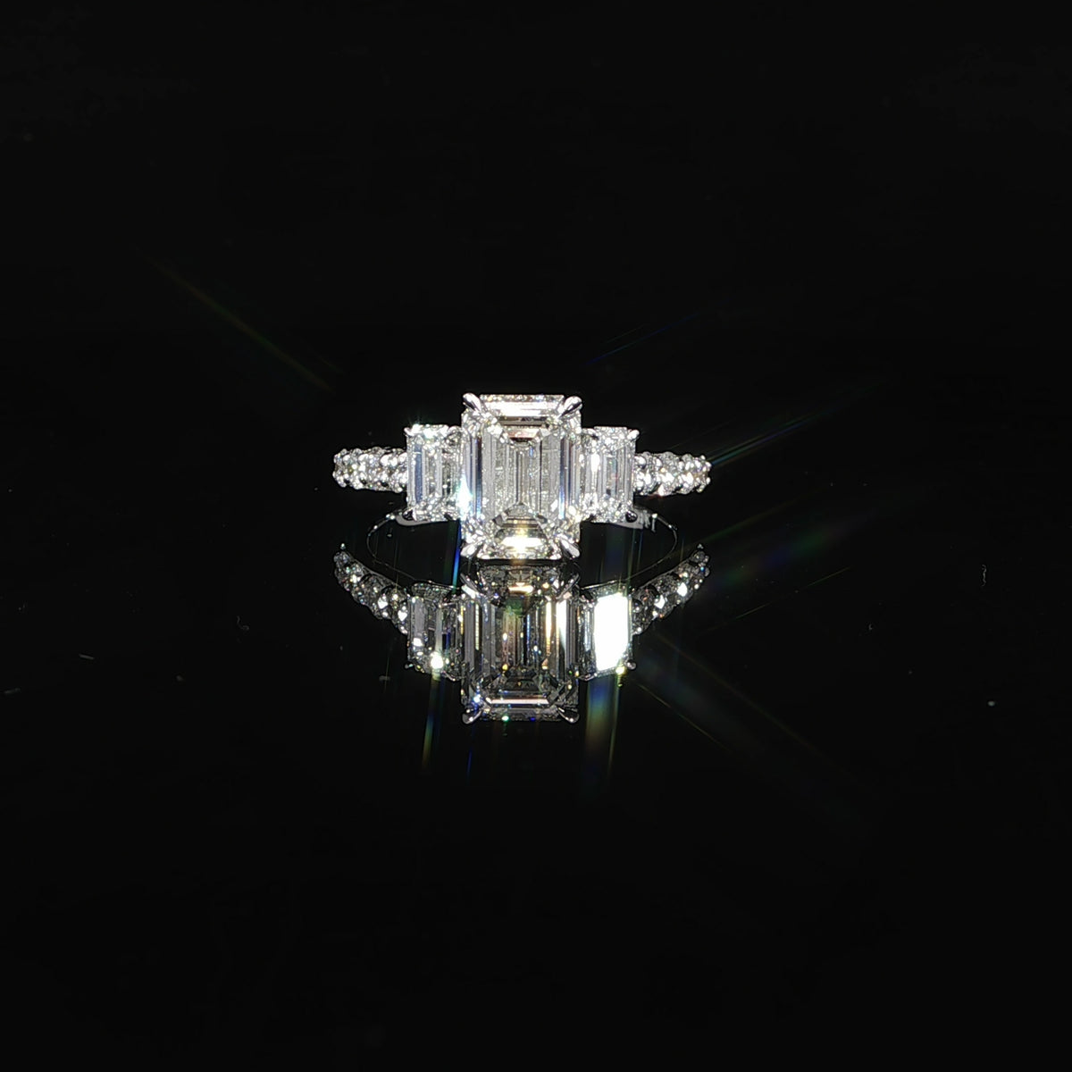 Front view of an emerald cut three-stone engagement ring in 14K white gold with pavé diamond accents.