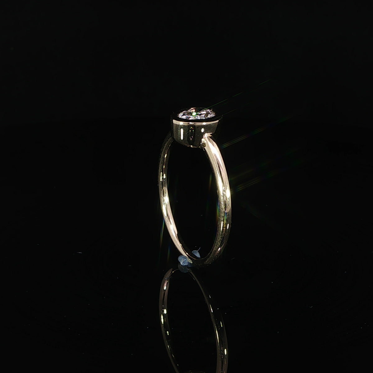 Side view of an oval bezel set diamond ring showing its low-profile setting and slim yellow gold band.