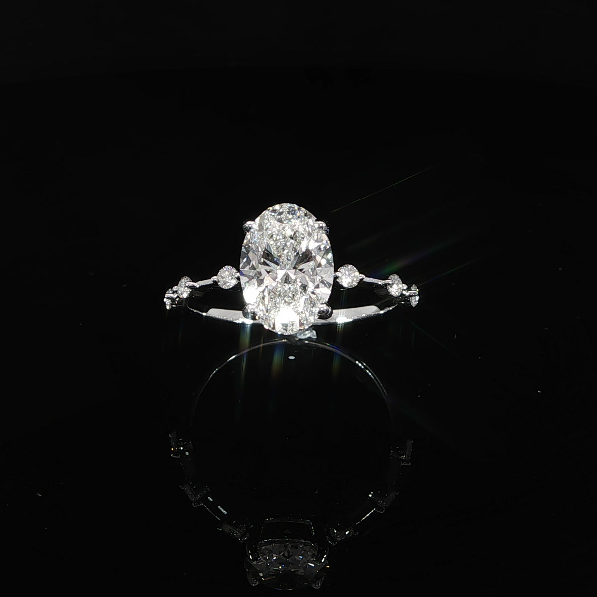 Top view of an oval diamond engagement ring with spaced round diamonds along the band.