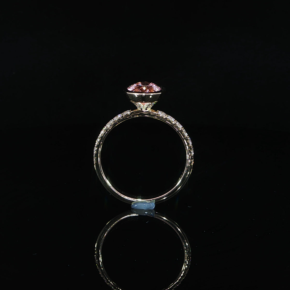 Ring resting on its side, revealing the bezel profile, supporting gallery, and diamond-set shoulders.