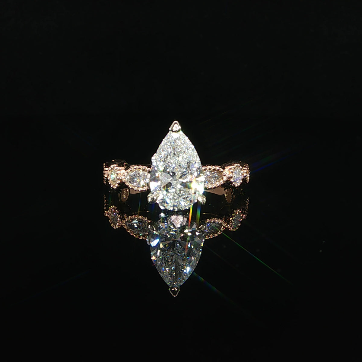 Front view of a pear cut diamond engagement ring in 14K rose gold with bezel set side diamonds.