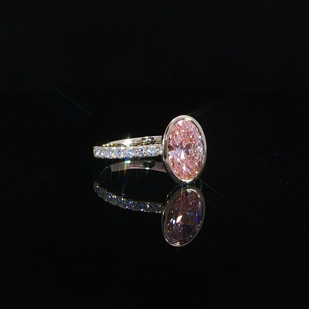 Yellow gold oval pink diamond ring reflected on a glossy black surface.
