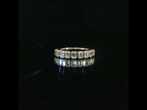 Emerald-cut diamond band in yellow gold with its reflection beneath the row of bezel-set stones.