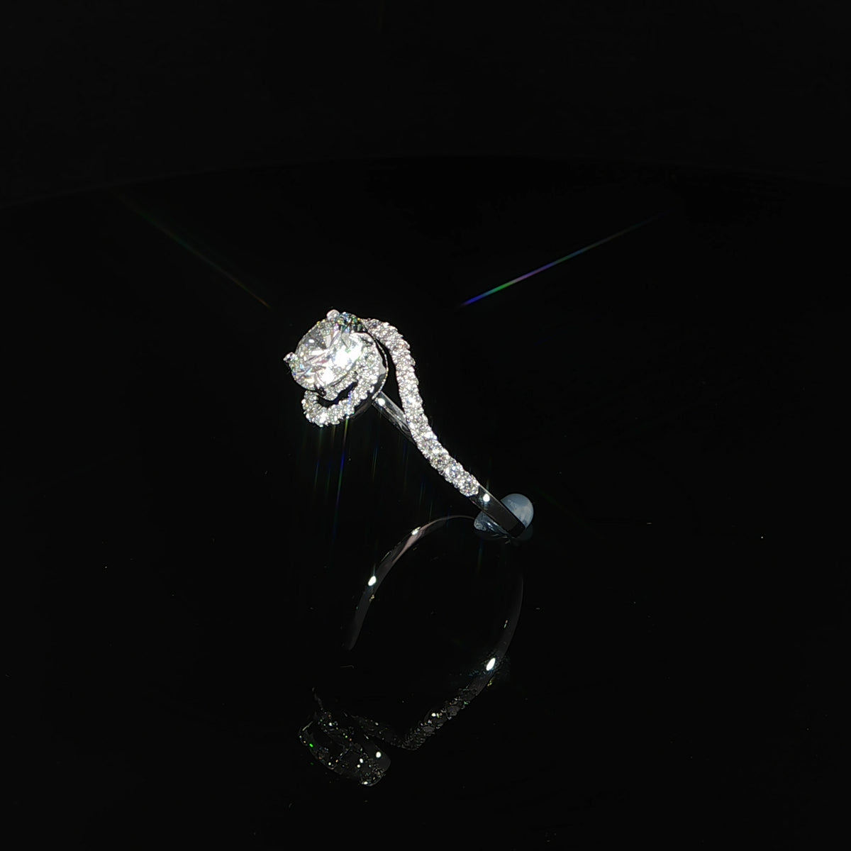 Front angle of a white gold engagement ring with diamond-set curves sweeping around the round center stone.