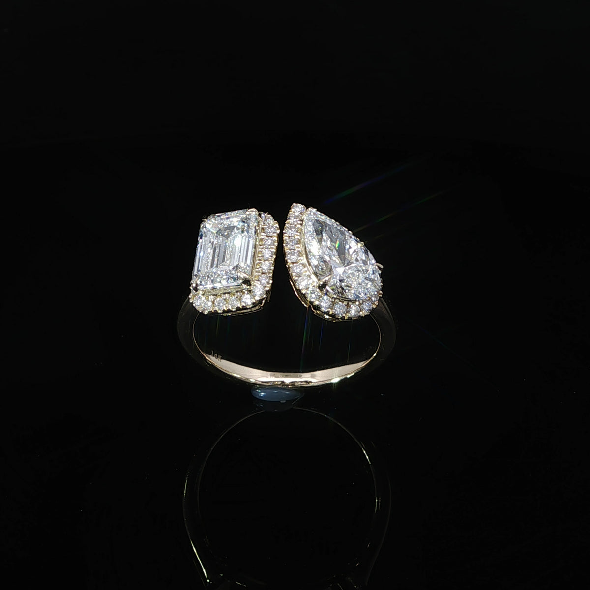Angled view of an open band Toi et Moi diamond ring with emerald and pear shaped center stones.