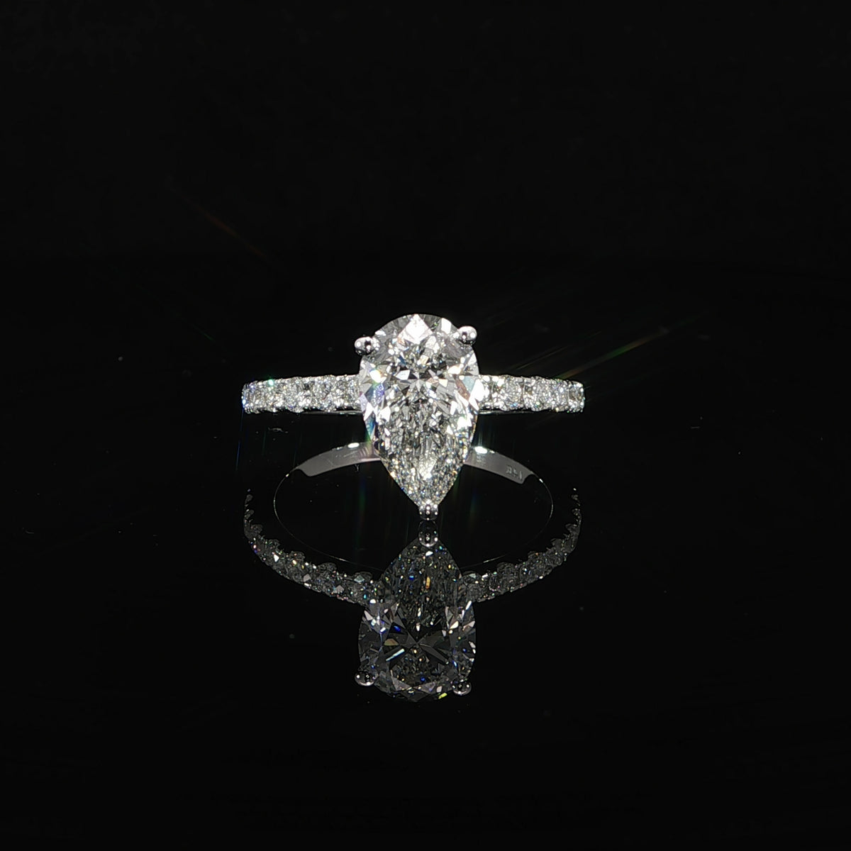 Front view of a pear diamond solitaire with a white gold pavé band, reflected on a black surface.