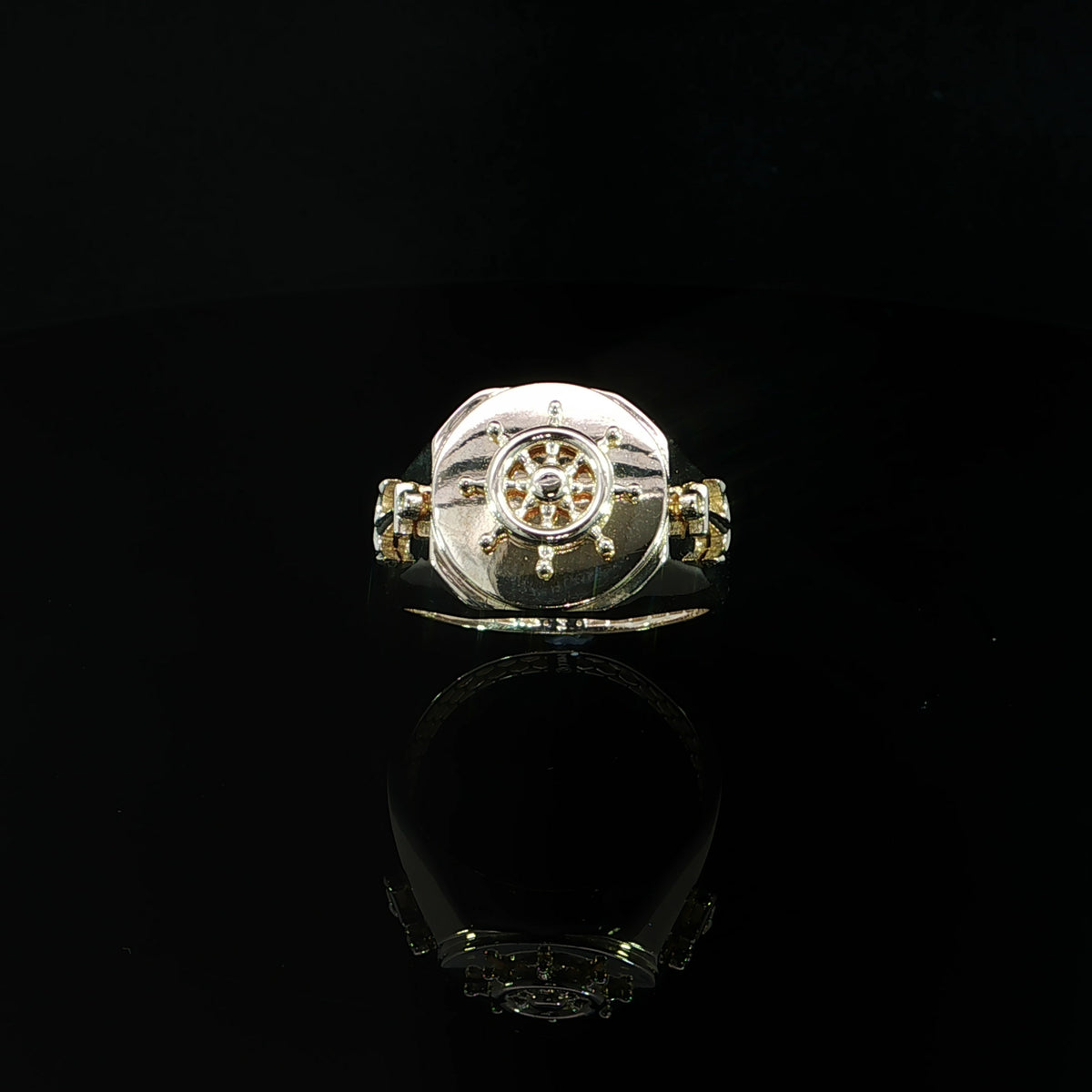 Angled view of a yellow gold nautical signet ring with a raised ship wheel, anchor detail and polished band.