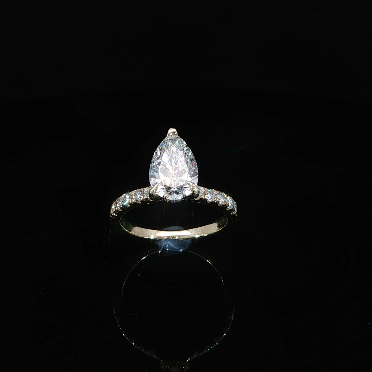 Top view of a yellow gold engagement ring featuring a pear-shaped center diamond and diamond-accented band.