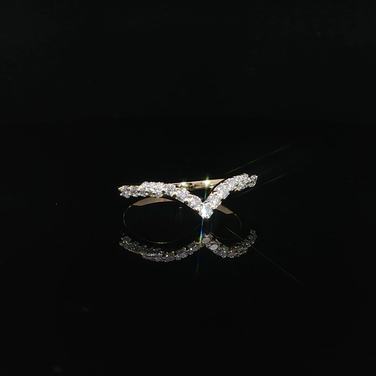 Round diamonds trace the V-shaped face of a yellow gold band, with small prongs visible along the edges.