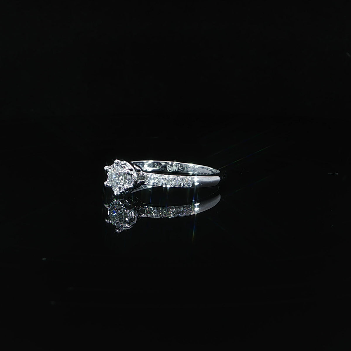 A 0.22 CTW natural diamond illusion ring in 10K white gold resting above its reflection on a black surface.