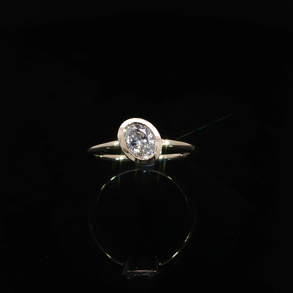 Angled view of a 0.70 carat oval diamond engagement ring with a smooth yellow gold bezel setting.