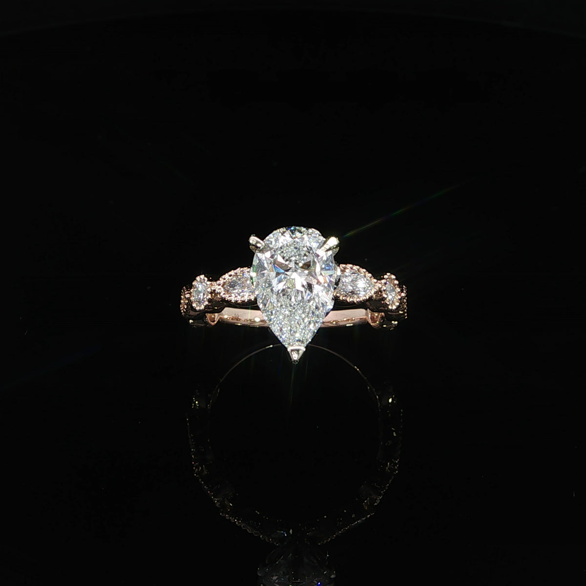 14K rose gold engagement ring with a 2 carat pear lab grown diamond and bezel set side stones.