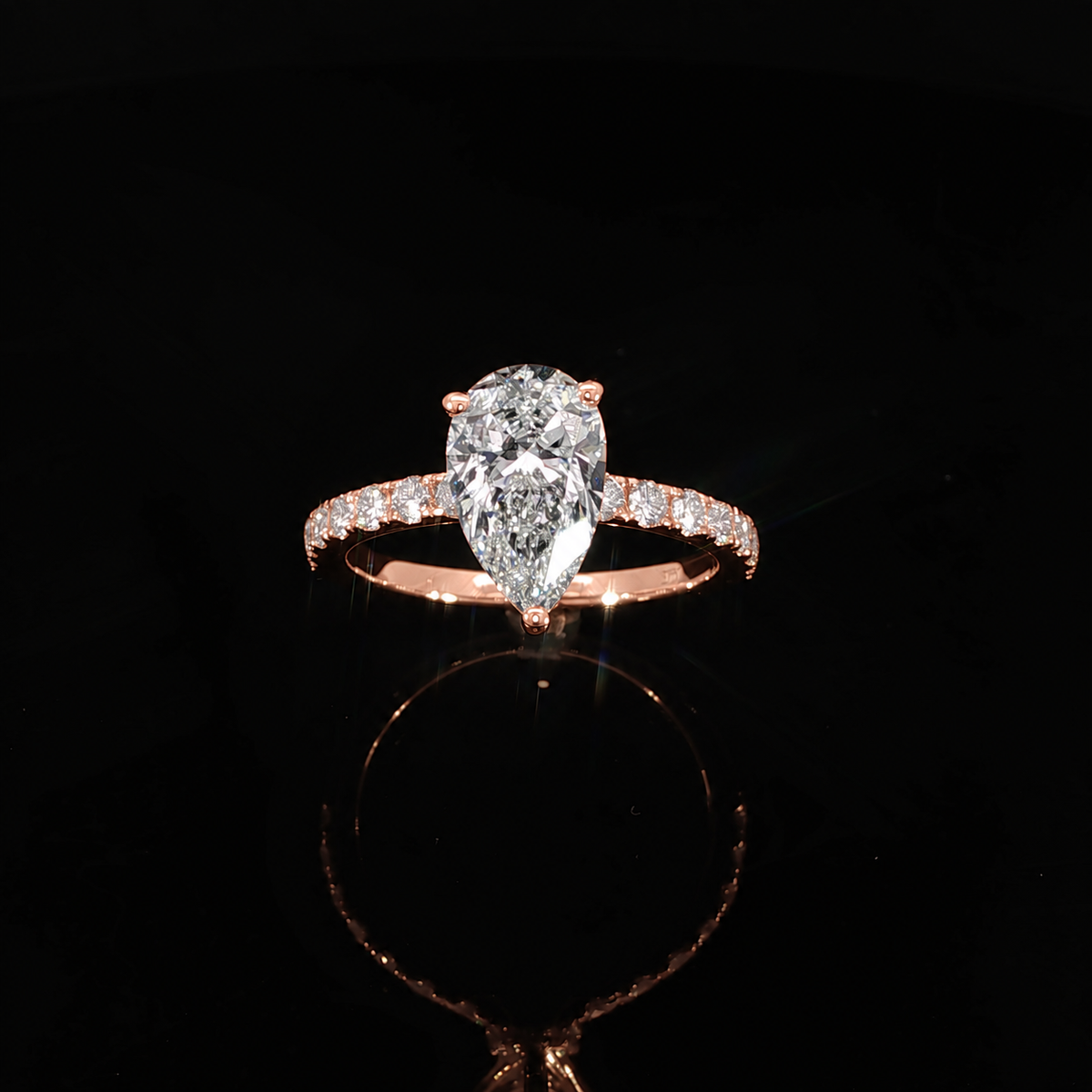 Front angle of a rose gold engagement ring with a pear center diamond and pavé-set shoulders.