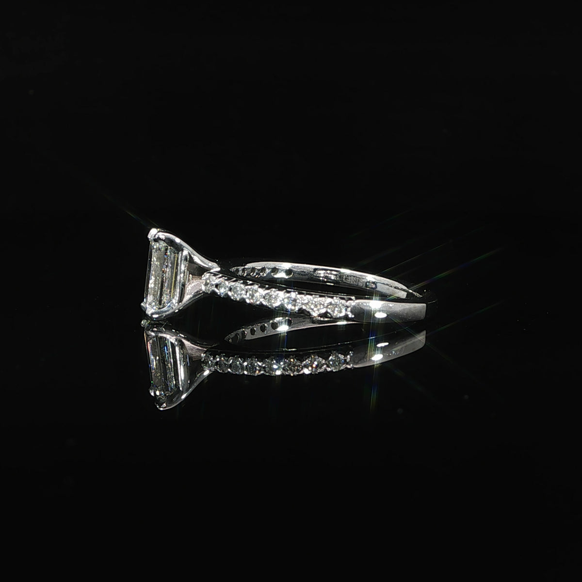 Resting side view of a 1.30 CTW emerald-cut diamond ring in 14K white gold, reflected on black.