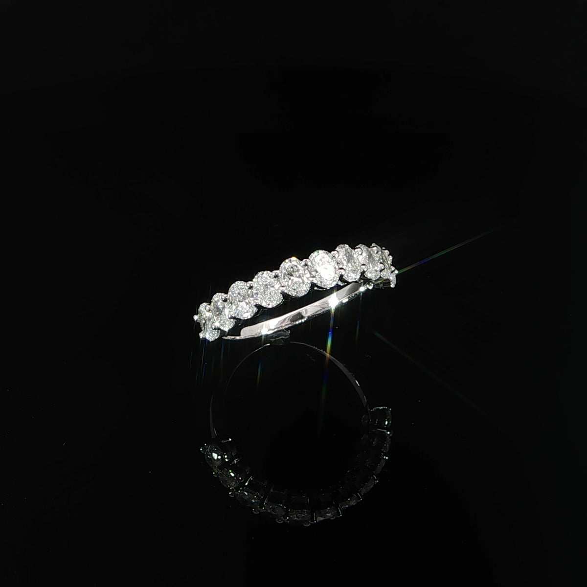 Angled view of a 14K white gold half eternity band with oval lab-grown diamonds.