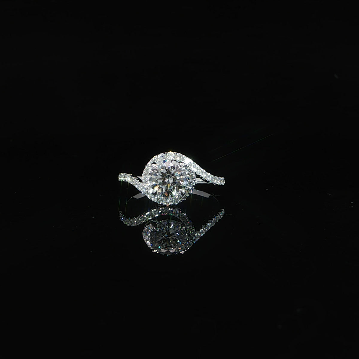 Front view of a white gold round diamond bypass ring reflected on a black surface.