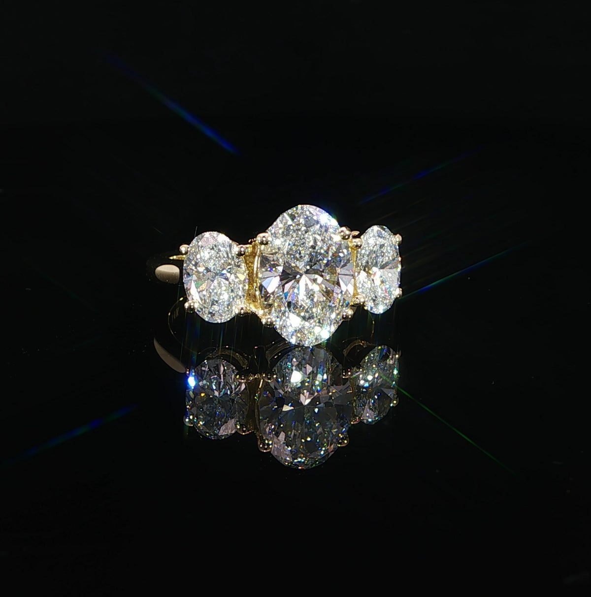 Front view of a 14K yellow gold three-stone ring with a 2.50-carat oval lab-grown center diamond and two oval side diamonds.