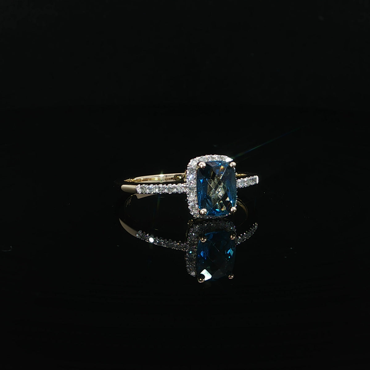 Angled view of a 14K yellow gold blue topaz ring with a diamond halo and 0.09 CTW diamonds.