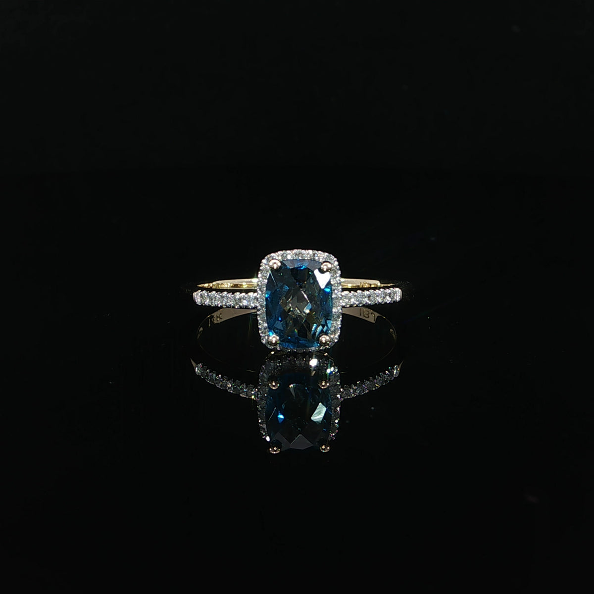 Front view of a 14K yellow gold blue topaz ring with 0.09 CTW diamonds reflected on a black surface.