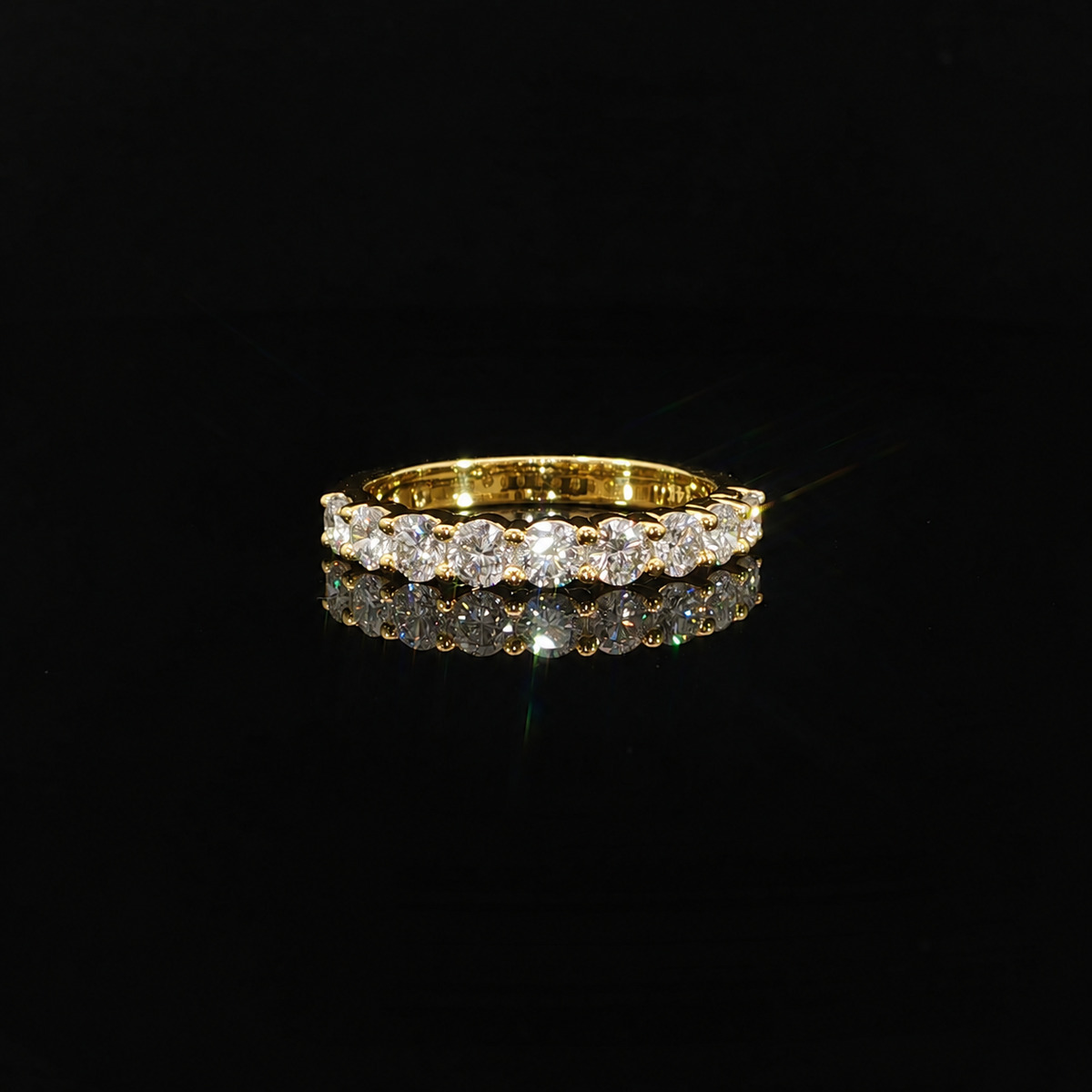 Round lab-grown diamonds held by polished gold prongs, reflected on a black surface.
