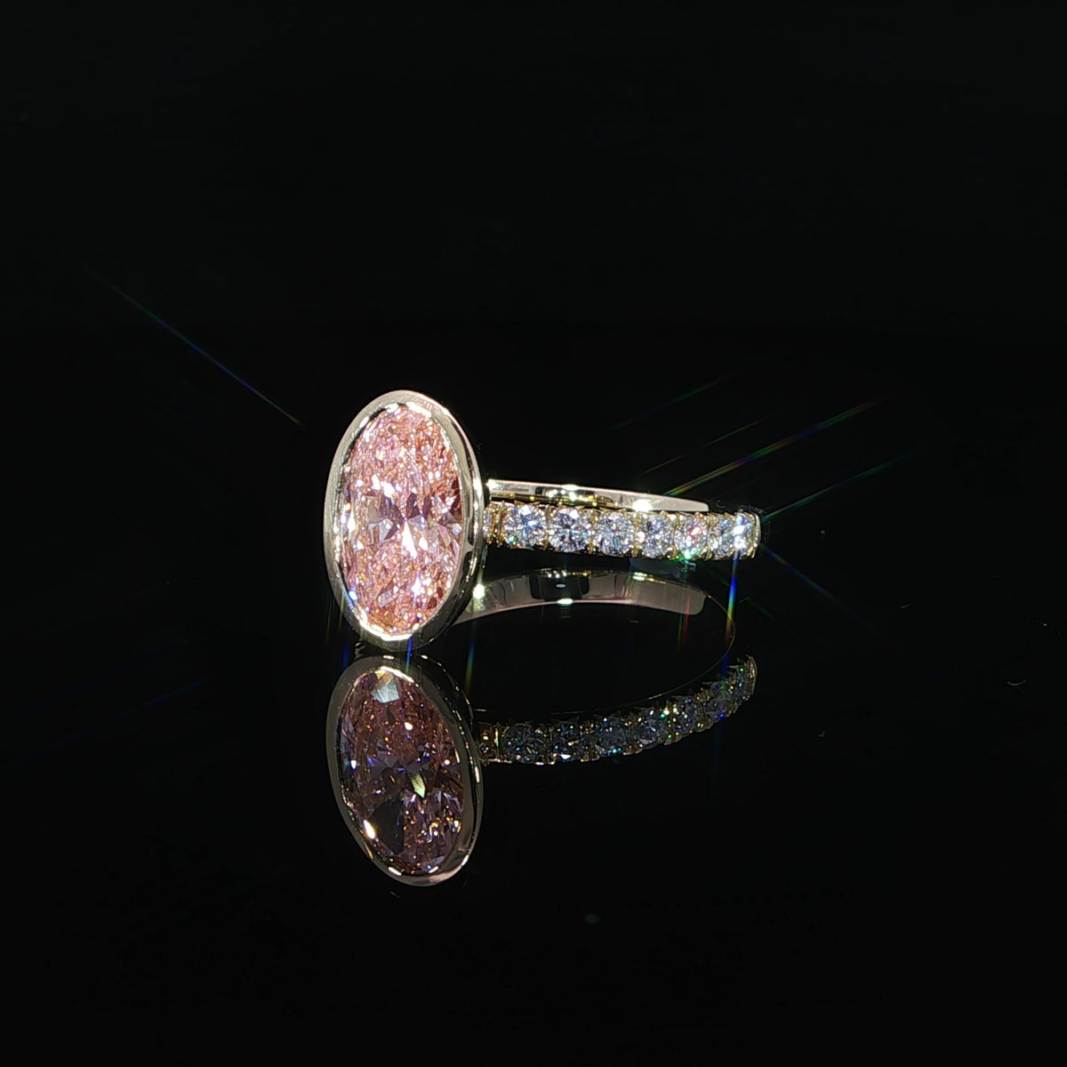 Side angle of a pink diamond ring showing the raised bezel setting and diamond-accented yellow gold band.