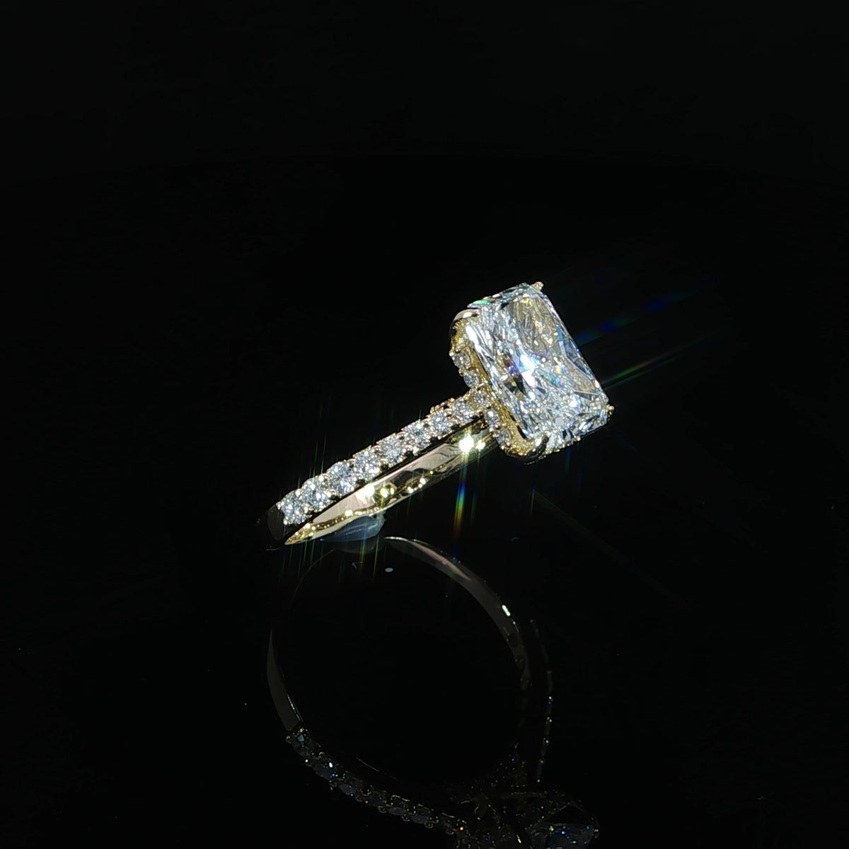 Side view of a yellow gold radiant diamond ring resting on a reflective surface
