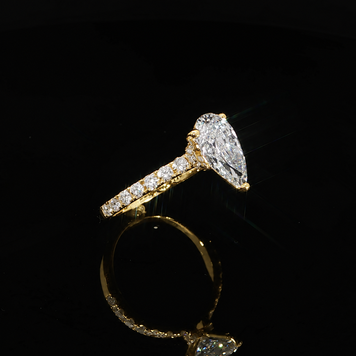 Side angle of a yellow gold engagement ring with a pear center diamond and pavé-set shoulders.