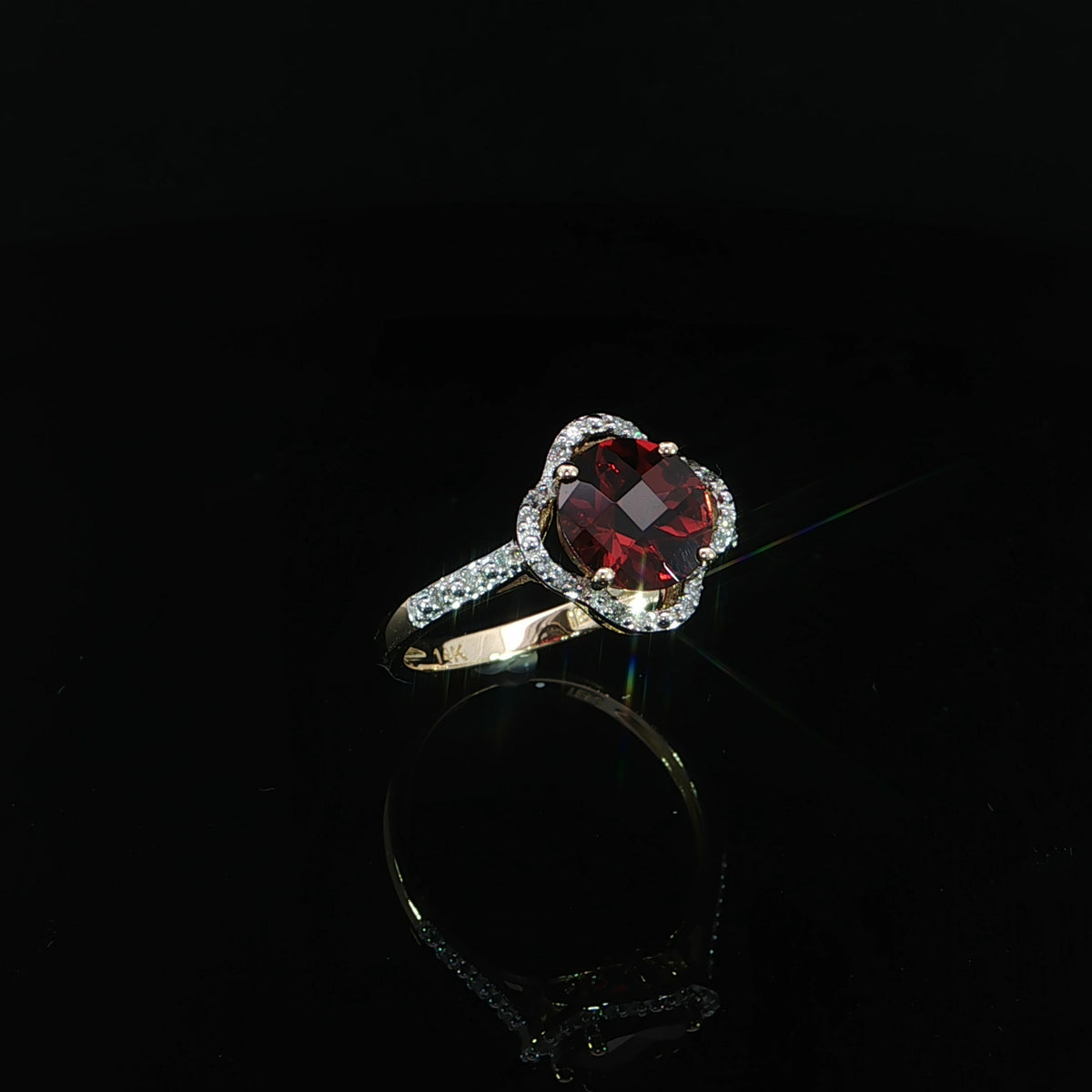 Angled view of a 14K yellow gold red garnet ring with a scalloped halo and 0.10 CTW diamonds.