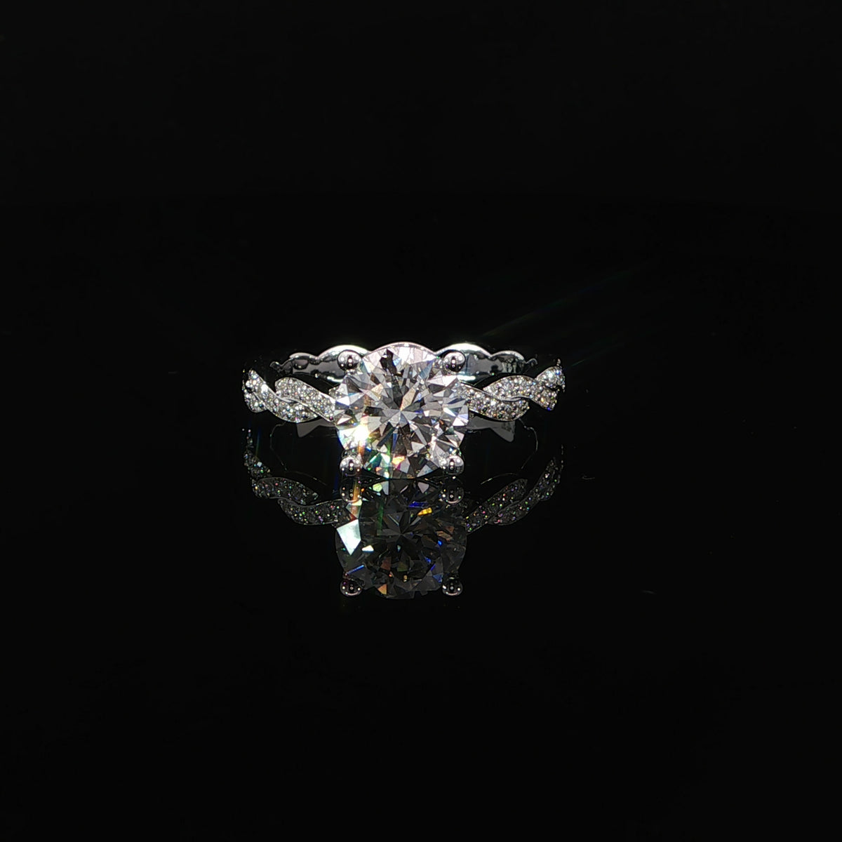 Front view of a round diamond ring with intertwined pavé shoulders, reflected on a black surface.