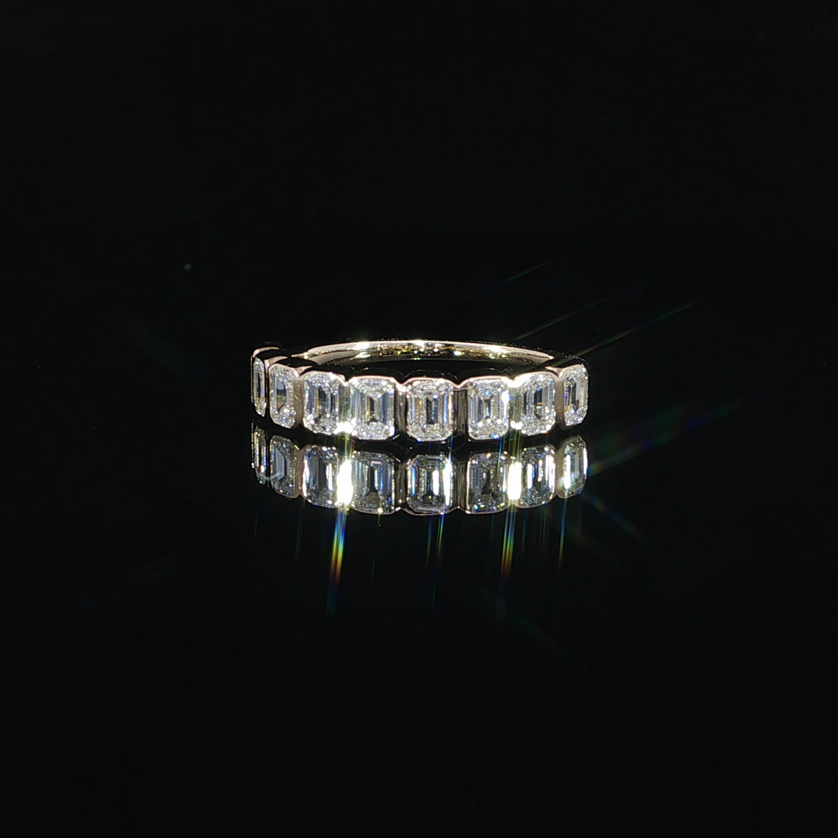 Front view of a half-eternity band with vertically oriented emerald-cut diamonds framed by yellow gold bezels.