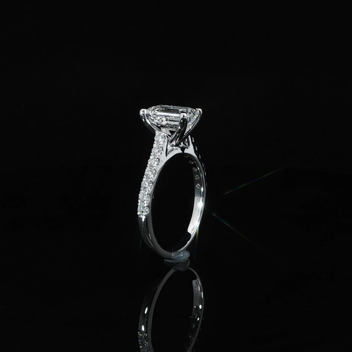 Side profile of an emerald cut diamond engagement ring showing the raised cathedral setting and pavé shoulders.