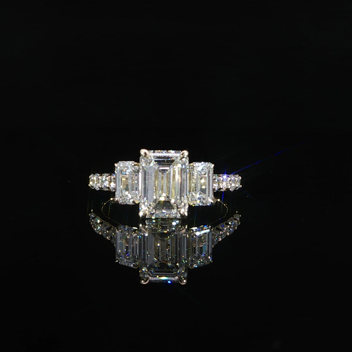 Front view of an emerald cut three-stone engagement ring in 14K yellow gold with pavé diamond accents.