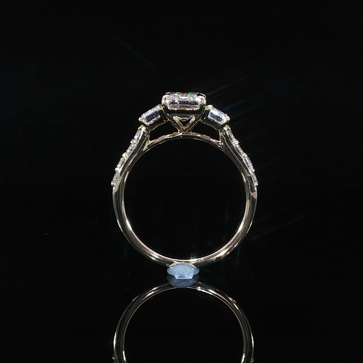 Side profile of an emerald cut three-stone diamond ring showing the raised center and side stone settings.
