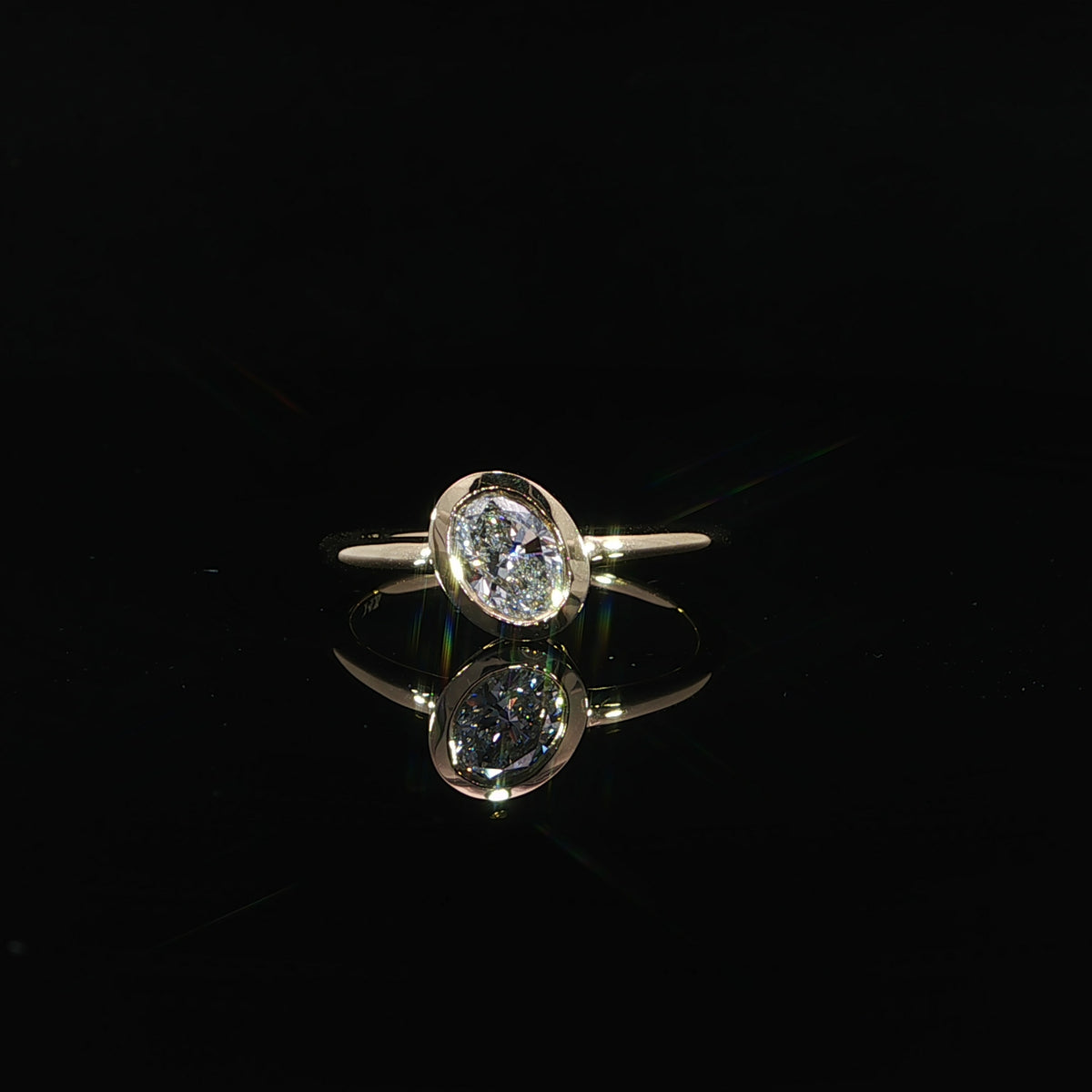 Front view of an oval bezel set diamond engagement ring in polished 14K yellow gold.