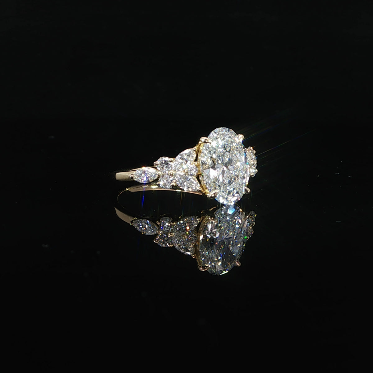 Oval center diamond engagement ring with marquise and round side accents set in polished yellow gold.