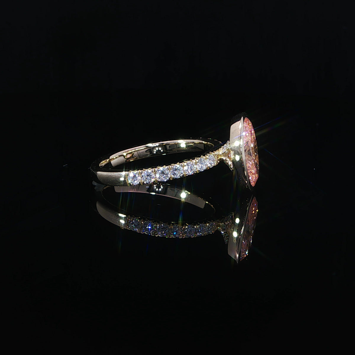 Ring resting on its side, revealing the bezel profile, supporting gallery, and diamond-set shoulders.