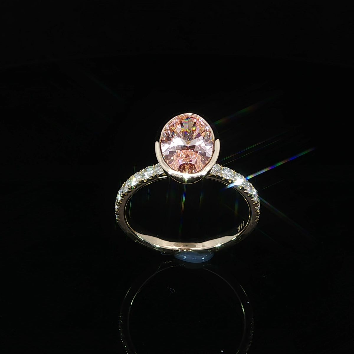 Front angle of an oval pink diamond in a yellow gold bezel with white diamonds along the band.