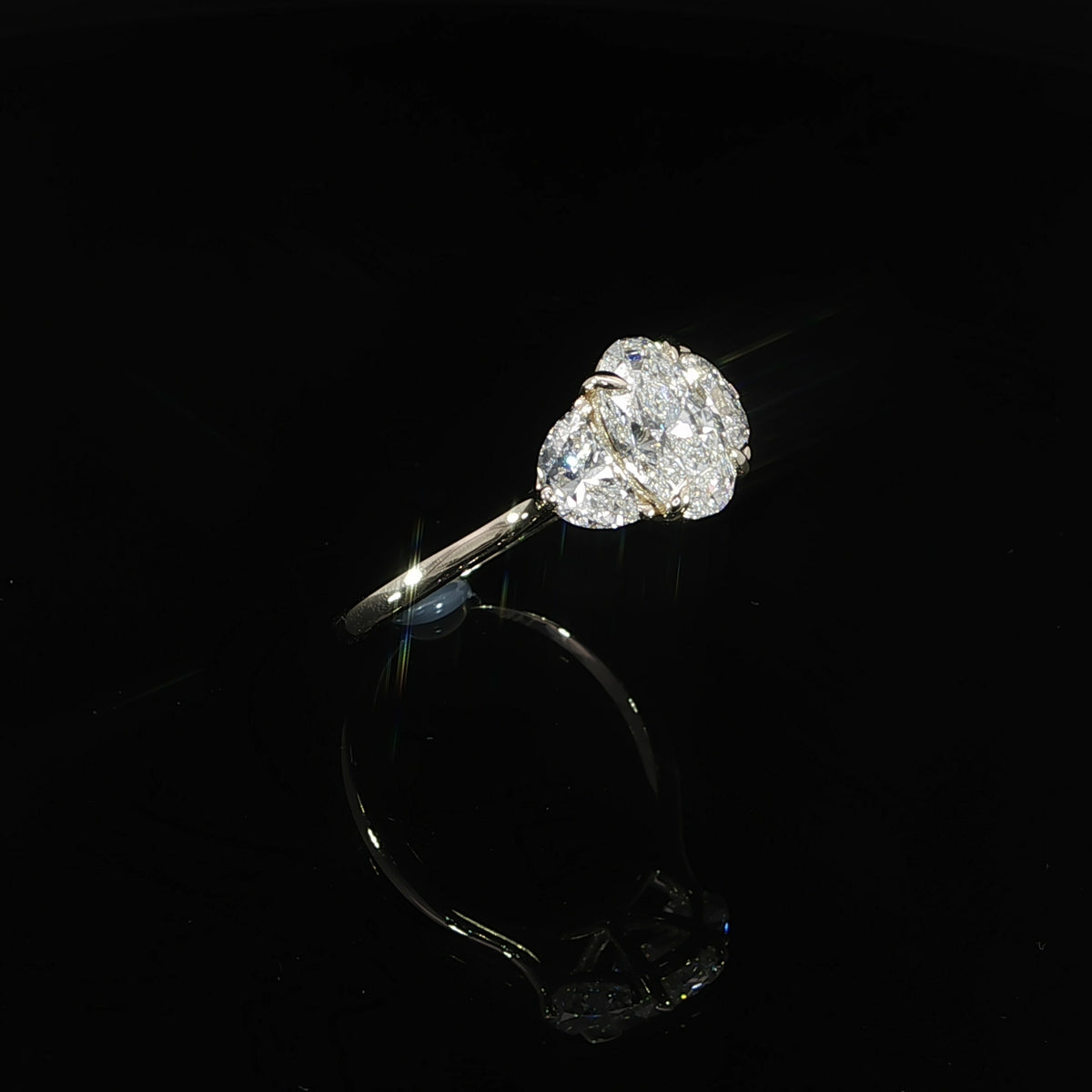 Side profile of an oval three-stone engagement ring showing its raised center setting and half-moon side diamonds.
