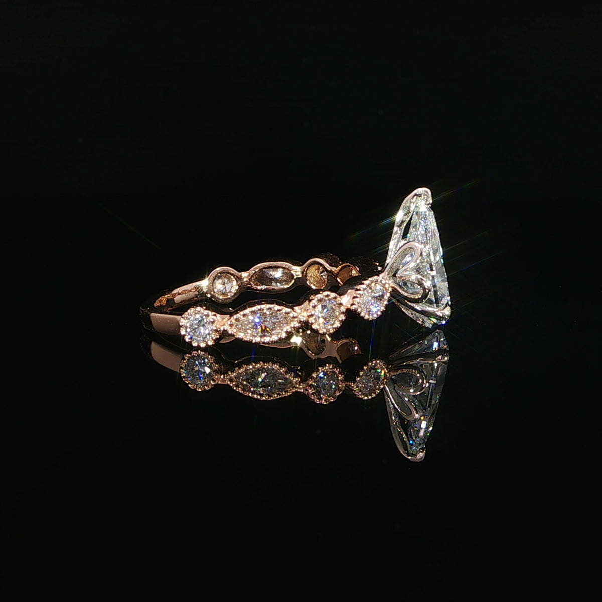 Close detail of a pear lab grown diamond engagement ring with bezel set diamond accents along the rose gold band.