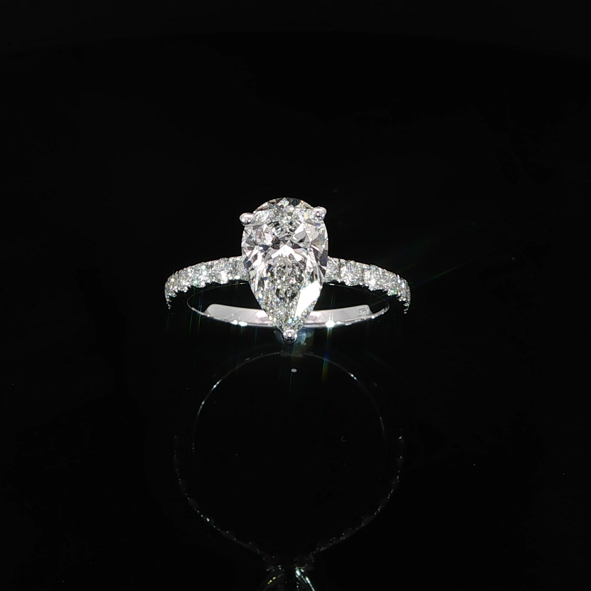 Front angle of a white gold engagement ring with a pear center diamond and pavé-set shoulders.